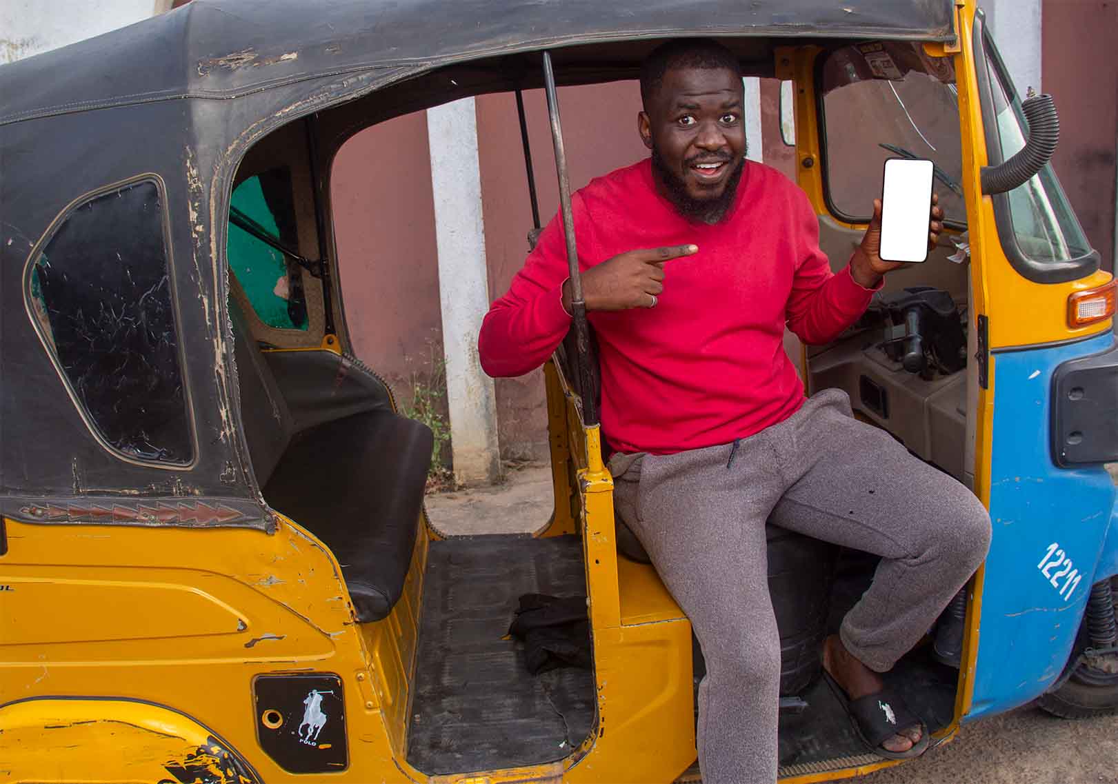 A happy African tricycle rider, also known as Keke or Maruwa, Keke rider, sitting in a tricycle  pointing at his phone